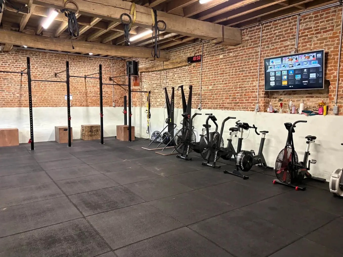 Intérieur de la salle Castle Training : murs en briques, poutres en bois, racks, bikes et rameurs